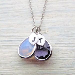 May include: A silver necklace with two teardrop-shaped pendants. The pendants are made of clear and purple glass and have silver charms with the letters "J" and "T" on them.