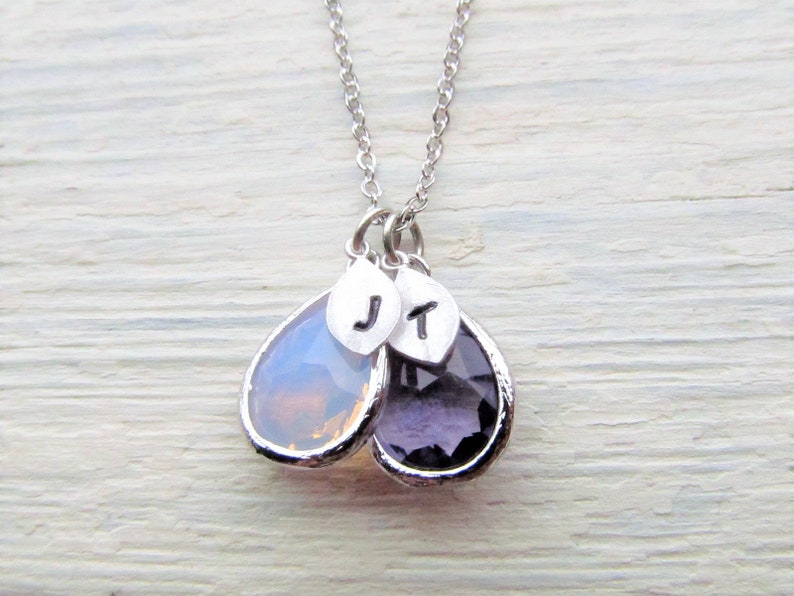 May include: A silver necklace with two teardrop-shaped pendants. The pendants are made of clear and purple glass and have silver charms with the letters "J" and "T" on them.