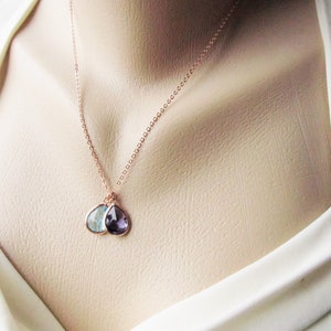 May include: A rose gold necklace with two teardrop-shaped pendants. The pendants are made of clear and purple gemstones.