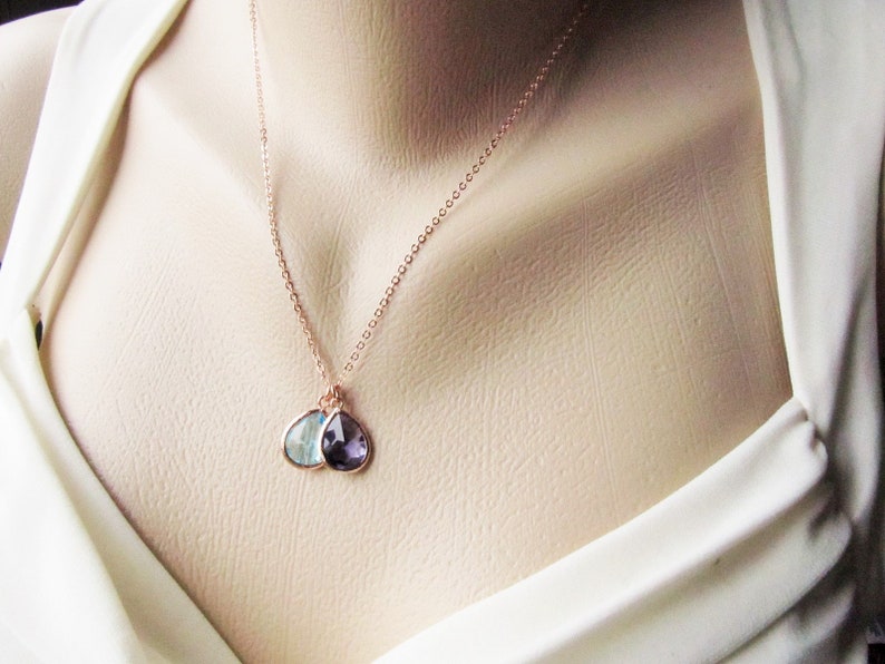 May include: A rose gold necklace with two teardrop-shaped pendants. The pendants are made of clear and purple gemstones.