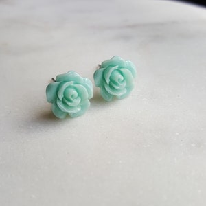May include: A pair of light blue rose stud earrings. The earrings are made of a smooth, shiny material and have a delicate, feminine design.