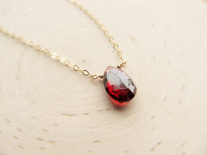 May include: A delicate gold chain necklace with a single, teardrop-shaped red gemstone pendant.