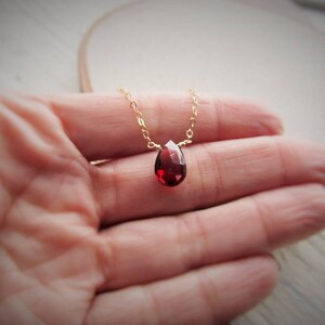 May include: A delicate gold chain necklace with a single teardrop-shaped red gemstone pendant.