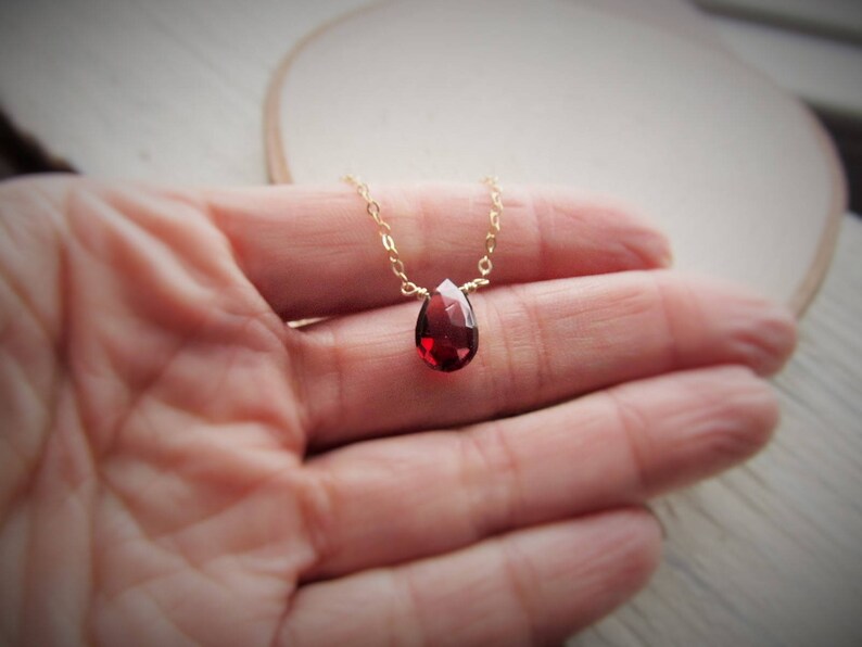 May include: A delicate gold chain necklace with a single teardrop-shaped red gemstone pendant.