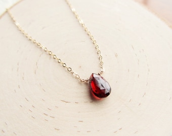 May include: A delicate gold chain necklace with a single, teardrop-shaped red garnet pendant.