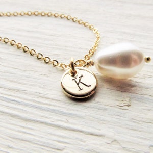 May include: A gold chain necklace with a small gold disc charm engraved with the letter "K" and a white pearl pendant.