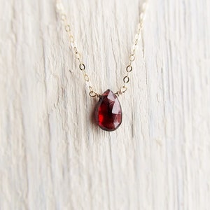May include: A delicate gold chain necklace with a single teardrop-shaped red gemstone pendant.