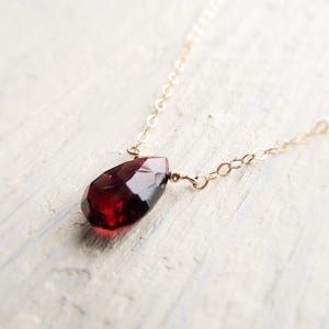 May include: A delicate gold chain necklace with a single, teardrop-shaped red garnet pendant.