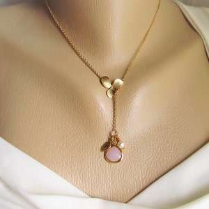 May include: A gold chain necklace with a pink stone pendant and a charm with three gold leaves. The necklace is on a white mannequin.