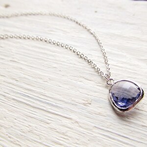 May include: A silver chain necklace with a purple gemstone pendant. The pendant is a faceted, irregular shape.