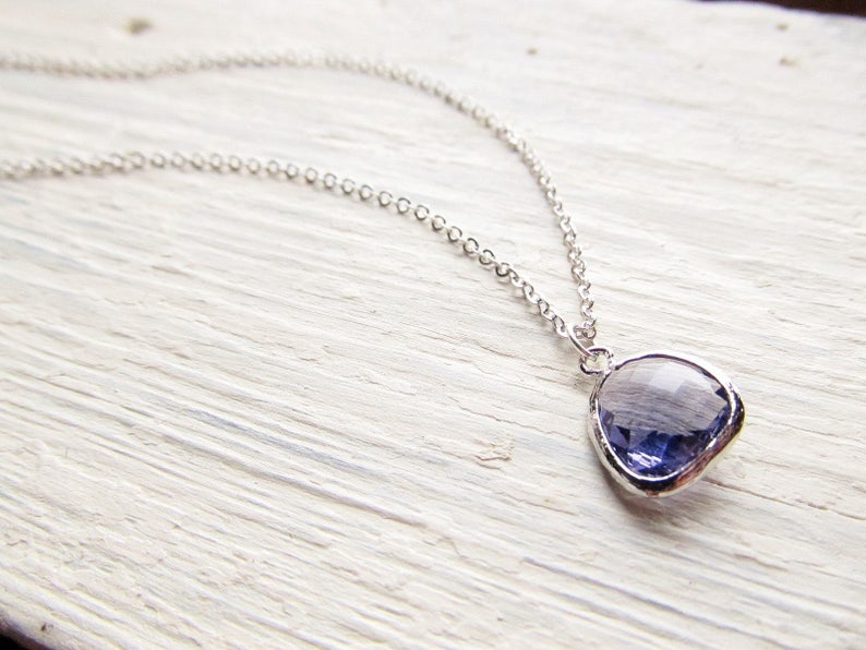 May include: A silver chain necklace with a purple gemstone pendant. The pendant is a faceted, irregular shape.