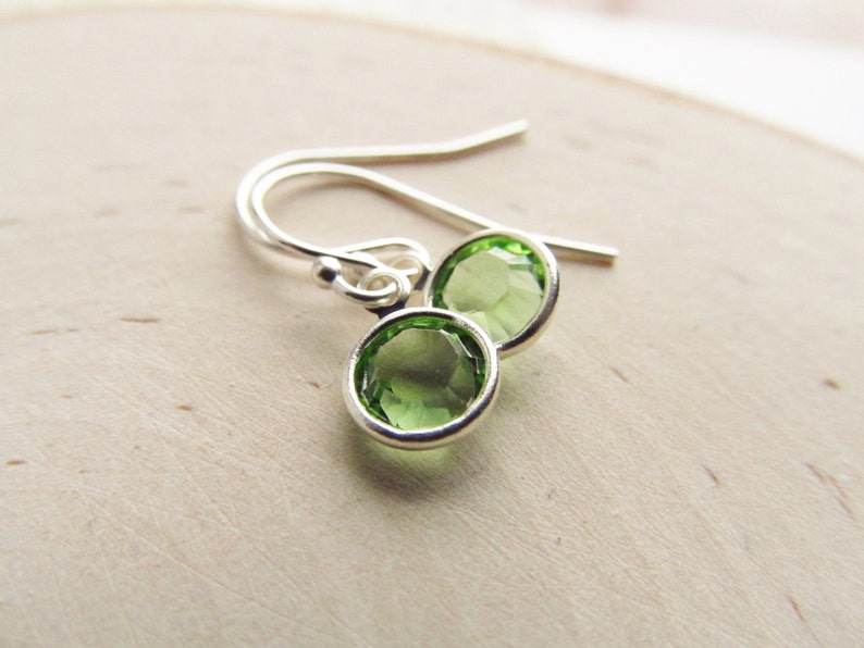 May include: A pair of silver earrings with green gemstone accents. The earrings have a simple, elegant design.