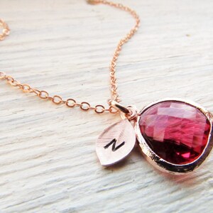 May include: A rose gold necklace with a pink teardrop-shaped gemstone pendant and a small leaf charm with the letter "N" engraved on it.