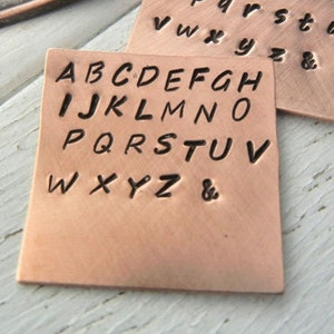 May include: A copper metal stamp with the alphabet in uppercase letters, including an ampersand symbol.