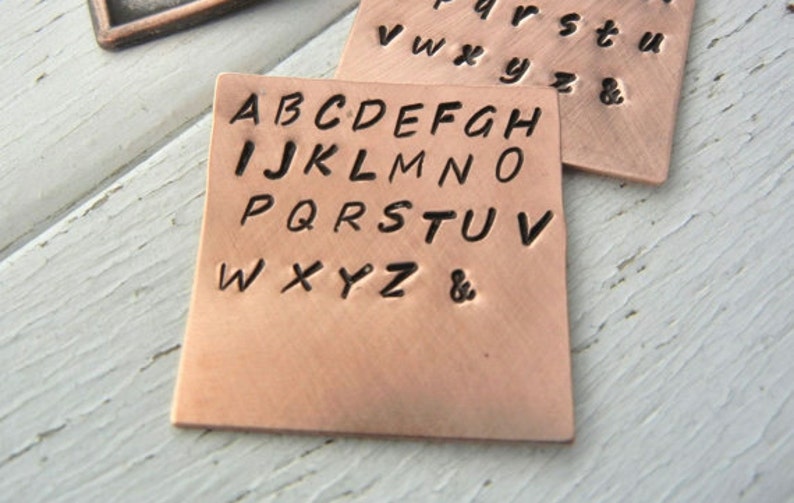 May include: A copper metal stamp with the alphabet in uppercase letters, including an ampersand symbol.