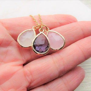 May include: A gold chain necklace with three teardrop-shaped pendants. The pendants are made of clear, pink, and purple glass.