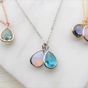 May include: Three silver necklaces with teardrop-shaped gemstone pendants. The necklaces feature different colored gemstones, including green, blue, pink, and purple.