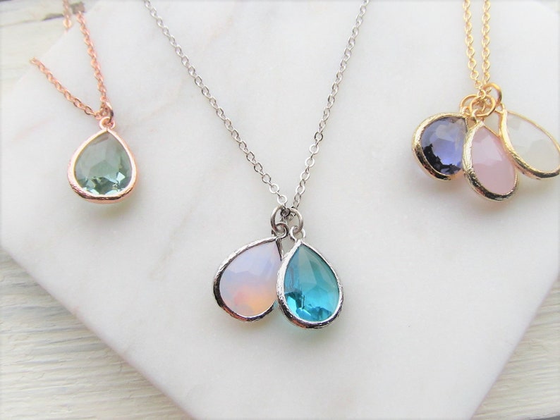 May include: Three silver necklaces with teardrop-shaped gemstone pendants. The necklaces feature different colored gemstones, including green, blue, pink, and purple.