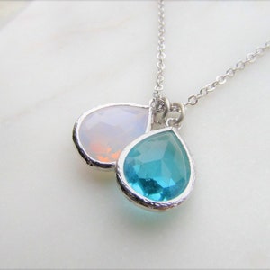 May include: A silver chain necklace with two teardrop-shaped pendants. The top pendant is a clear, iridescent opal, and the bottom pendant is a bright turquoise blue.