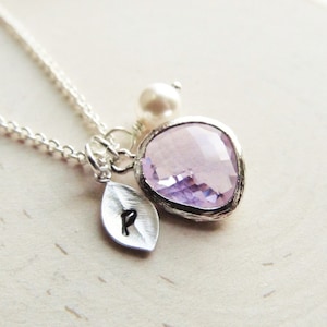 May include: A silver necklace with a delicate chain, a small pearl charm, a leaf charm with the letter "P" engraved on it, and a large, faceted, light purple gemstone pendant.