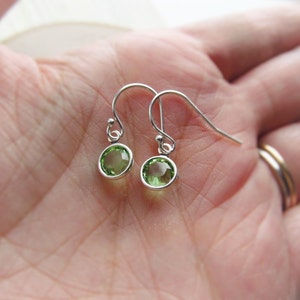 May include: A pair of silver dangle earrings with small, round, green gemstones.
