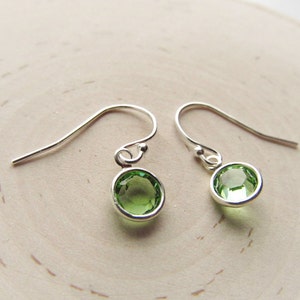 May include: A pair of silver dangle earrings with small, round, light green gemstones.