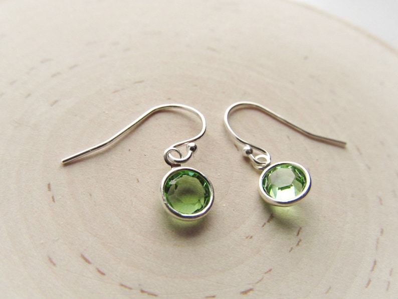 May include: A pair of silver dangle earrings with small, round, light green gemstones.