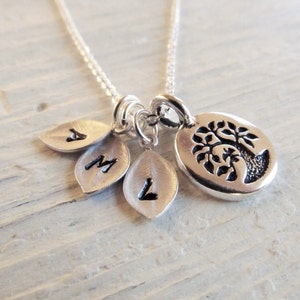 May include: Silver necklace with a tree charm and three leaf charms with the letters A, M, and L engraved on them.