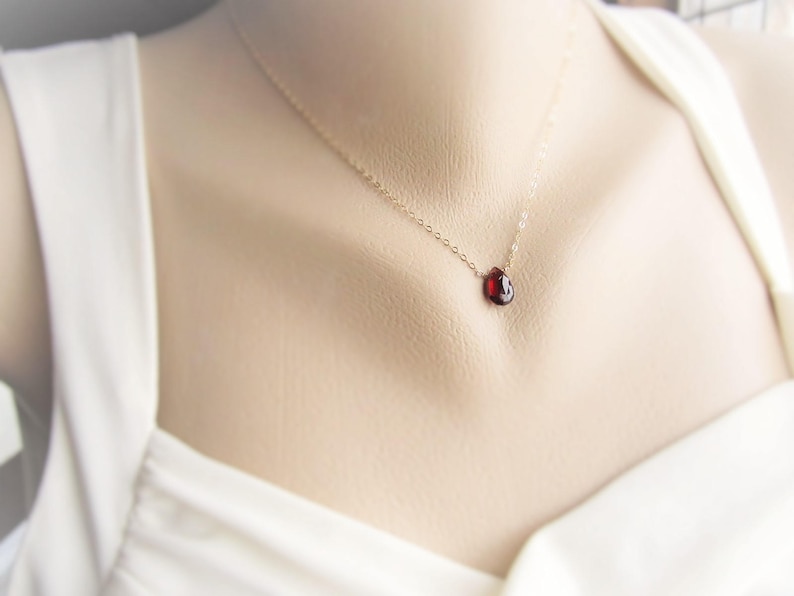 May include: A delicate gold chain necklace with a small, red gemstone pendant.