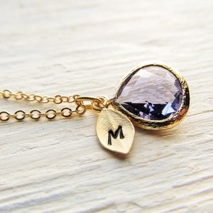 Peut inclure: Un collier en or avec un pendentif en forme de larme en pierre précieuse violette et un petit charme en feuille d'or gravé de la lettre 'M'.