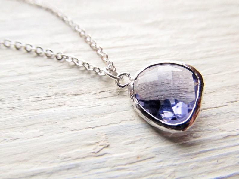 May include: A silver chain necklace with a light purple gemstone pendant. The pendant is shaped like a teardrop and has a faceted design.
