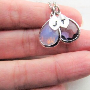 May include: A silver necklace with two teardrop-shaped pendants. The pendants are made of clear and purple glass and have silver initials "J" and "T" on them.