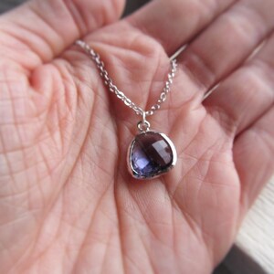 May include: A silver chain necklace with a purple gemstone pendant. The pendant is a rounded oval shape with a faceted surface.