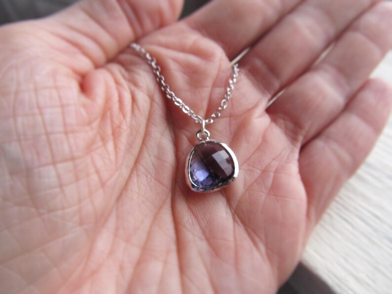 May include: A silver chain necklace with a purple gemstone pendant. The pendant is a rounded oval shape with a faceted surface.