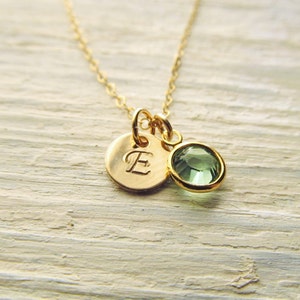 May include: A gold necklace with a small round pendant featuring the letter 'E' and a green gemstone.