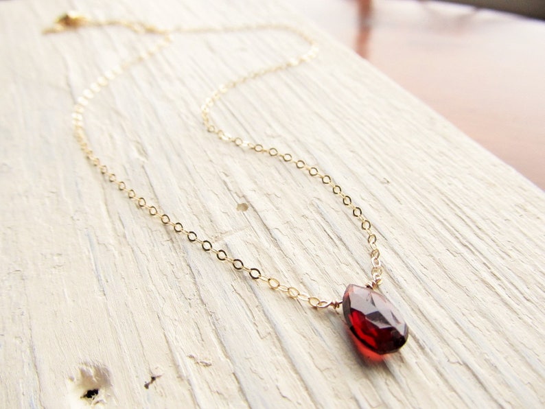 May include: A delicate gold chain necklace with a single, faceted, red gemstone pendant.
