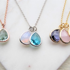 May include: Three delicate necklaces with teardrop-shaped crystal pendants. The necklaces are in gold, silver, and rose gold. The crystals are in shades of green, blue, purple, pink, and white.