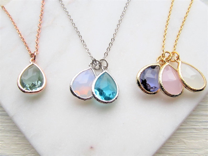 May include: Three delicate necklaces with teardrop-shaped crystal pendants. The necklaces are in gold, silver, and rose gold. The crystals are in shades of green, blue, purple, pink, and white.