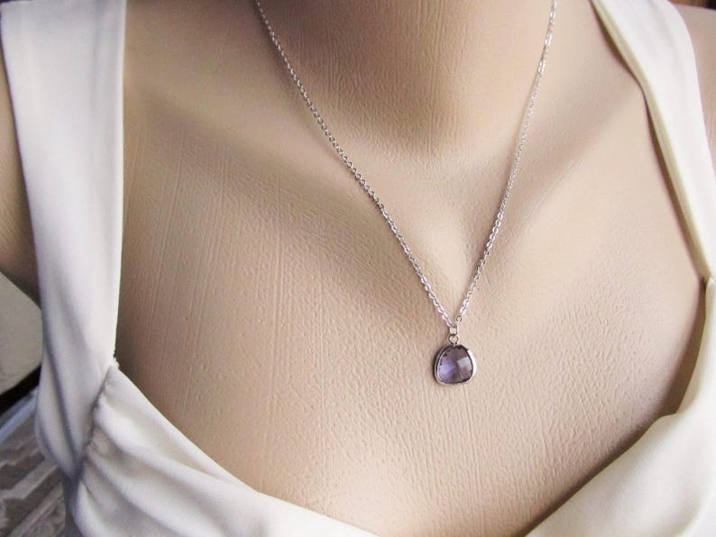 May include: A silver chain necklace with a small, faceted, purple gemstone pendant.