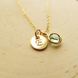 May include: A gold necklace with a small round pendant featuring the letter "E" and a green gemstone.