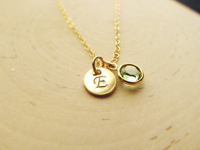May include: A gold necklace with a small round pendant featuring the letter "E" and a green gemstone.