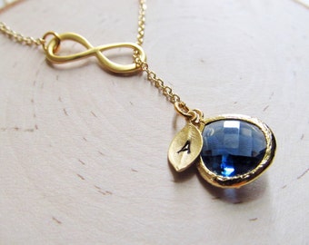 May include: Gold infinity necklace featuring a blue gemstone pendant and a small leaf charm with the letter 'A' engraved on it.
