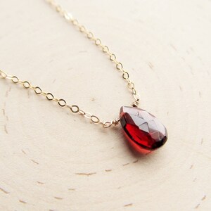 May include: A delicate gold chain necklace with a single, teardrop-shaped red gemstone pendant.