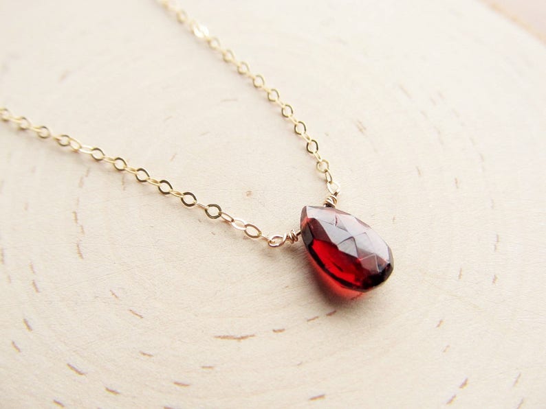 May include: A delicate gold chain necklace with a single, teardrop-shaped red gemstone pendant.