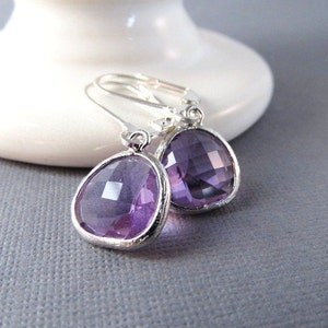 May include: A pair of silver dangle earrings with a purple gemstone. The earrings have a teardrop shape and are accented with a silver bezel.