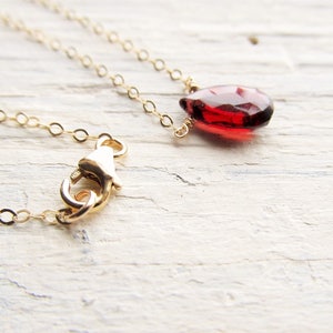 May include: A delicate gold chain necklace with a single, teardrop-shaped red gemstone pendant.