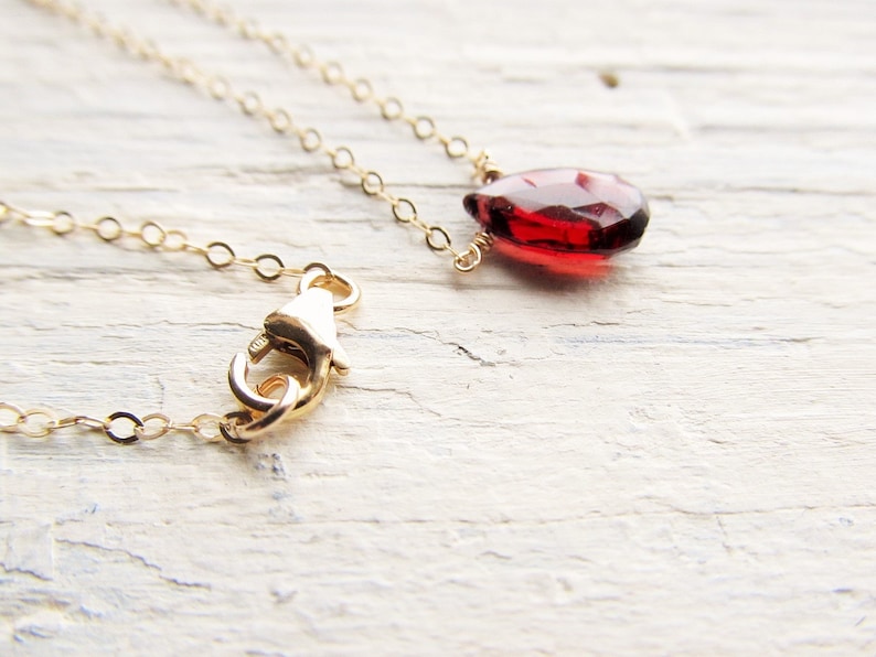May include: A delicate gold chain necklace with a single, teardrop-shaped red gemstone pendant.