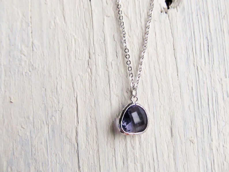May include: A silver chain necklace with a small, teardrop-shaped pendant featuring a dark purple gemstone.