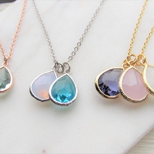 May include: Three delicate necklaces with teardrop-shaped pendants. The necklaces are made of gold, silver, and rose gold chains. The pendants are made of clear, blue, pink, and purple gemstones.