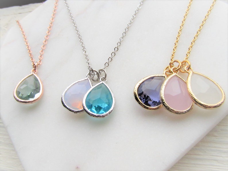 May include: Three delicate necklaces with teardrop-shaped pendants. The necklaces are made of gold, silver, and rose gold chains. The pendants are made of clear, blue, pink, and purple gemstones.